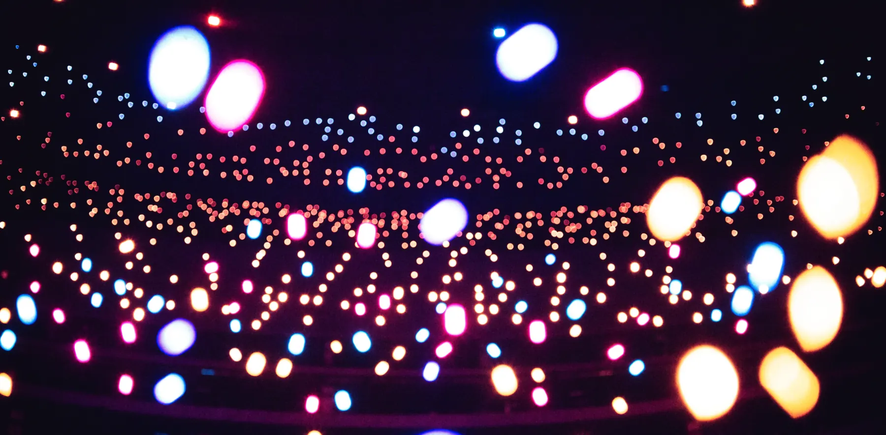 A dark arena filled with small out-of-focus lights in cyan, magenta and gold